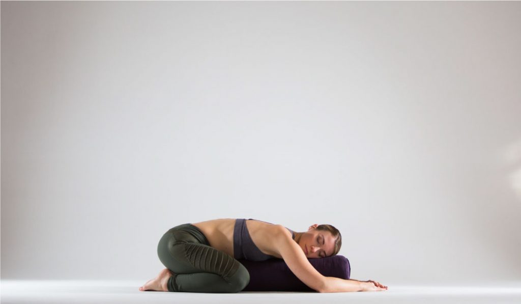 Mujer sobre cojin bolster de yoga restaurativo en postura del niño