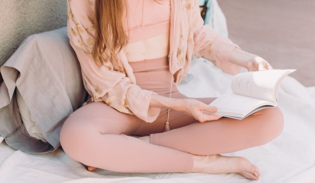 Chica vestida con ropa de yoga sentada leyendo libro