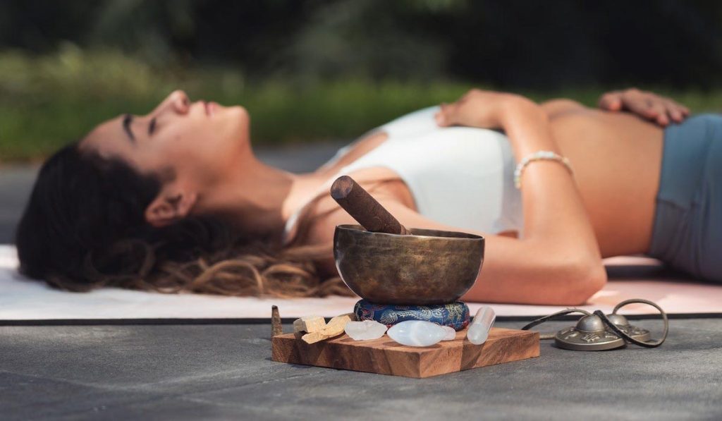 Chica tumbada practicando kundalini yoga con cuenco tibetano al lado