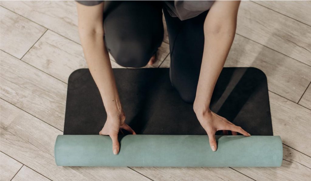 Manos de mujer desplegando esterilla de yoga en el suelo