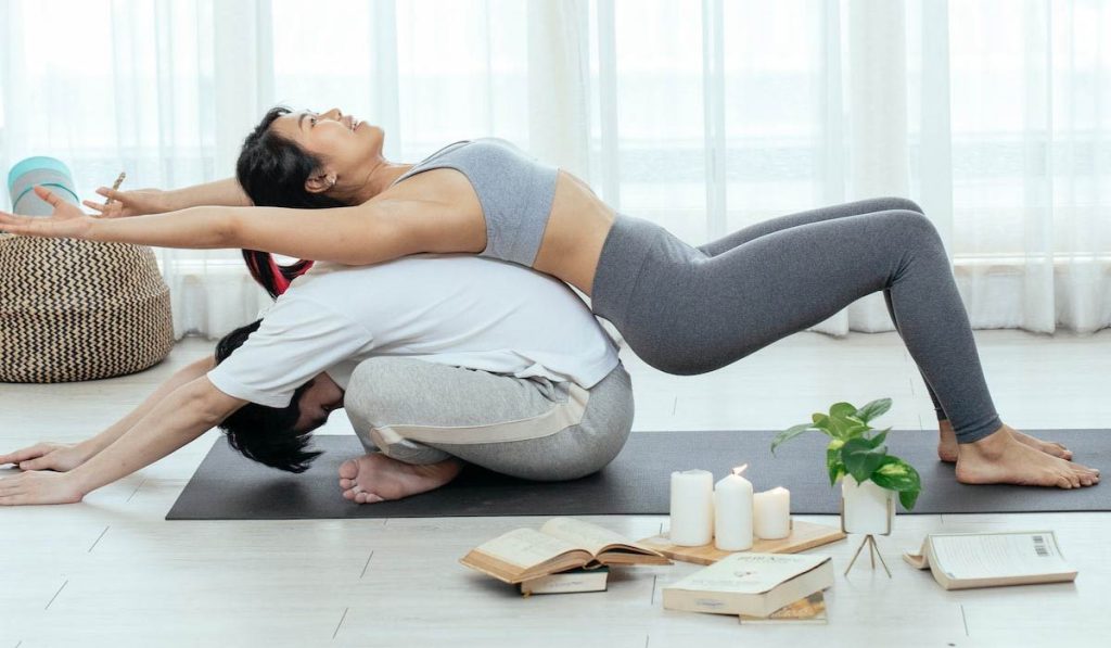 Chica y chica joven practicando yoga con libros de yoga para principiantes en el suelo