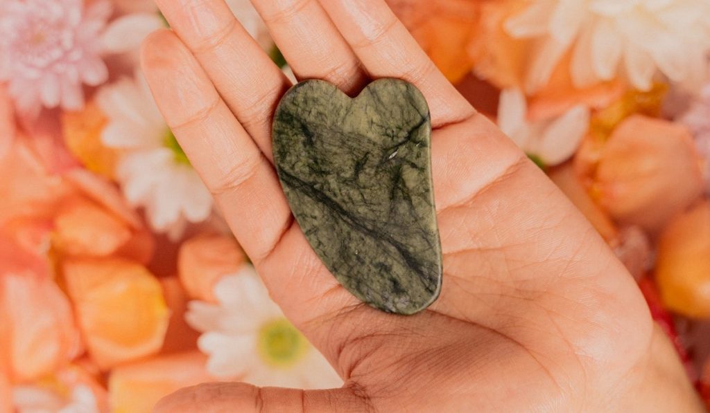 Piedra masajeadora facial gua sha original de jade posada en una mano