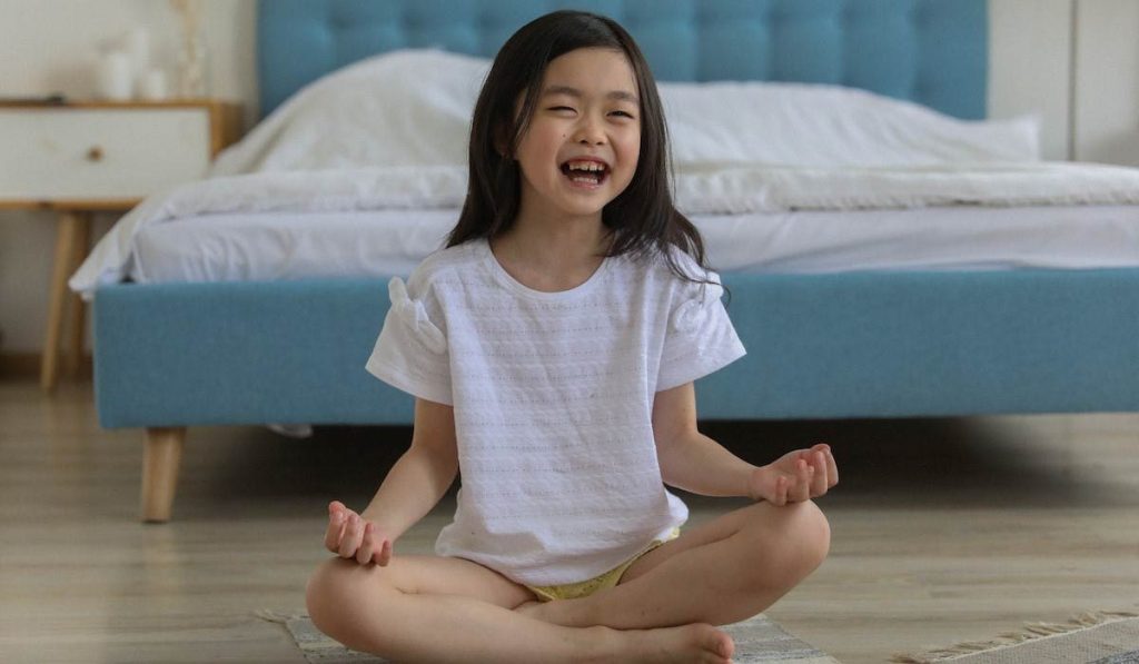 Niña haciendo yoga en posición sentada y riendo
